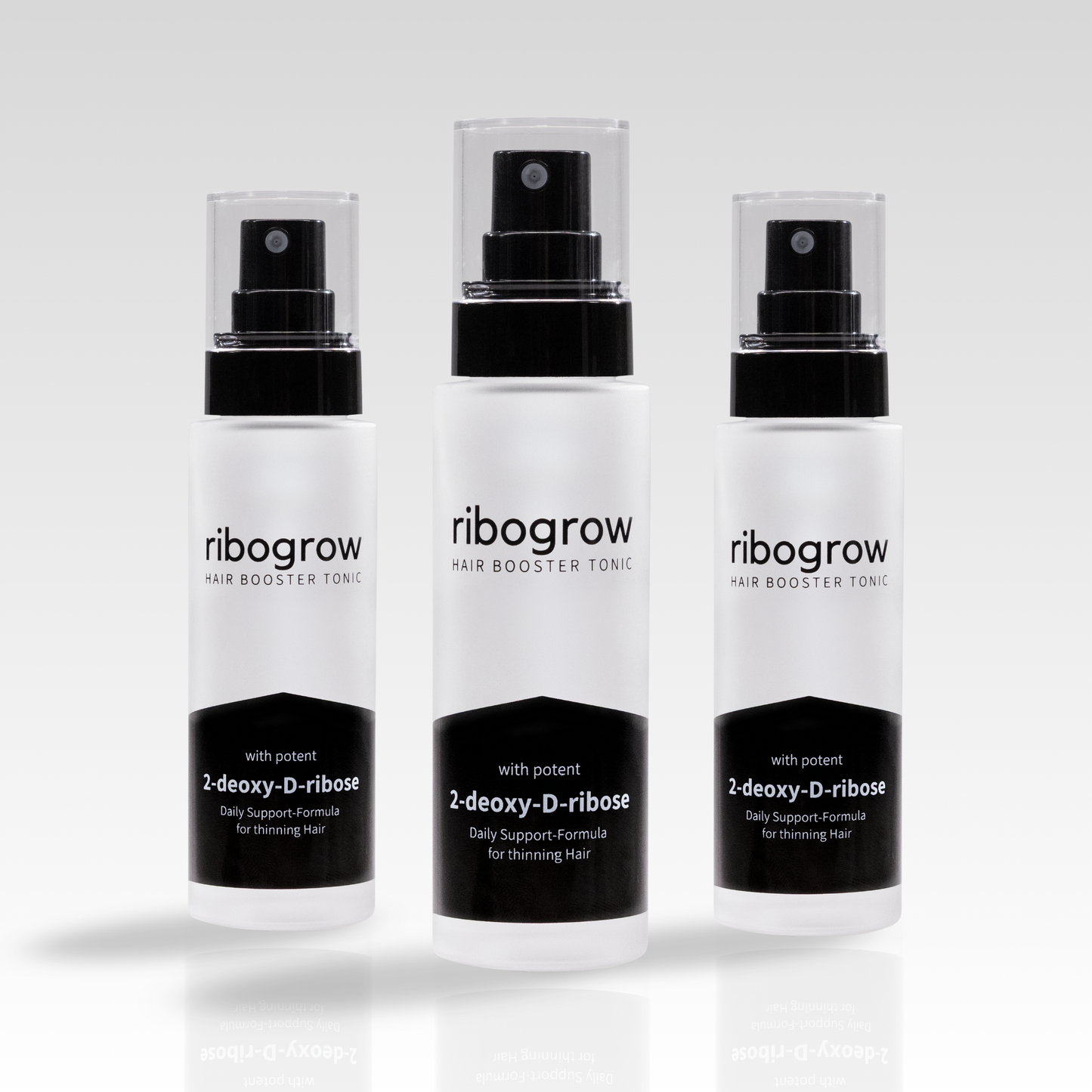 Drei Flaschen ribogrow Hair Booster Tonic aus mattem Glas mit schwarzem Sprühkopf und transparenter Kappe, nebeneinander auf hellem Hintergrund angeordnet.