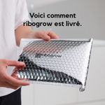 Une personne tient une enveloppe d’expédition argentée à bulles, ornée du logo ribogrow et d’un QR code. L’image présente l’emballage de livraison du ribogrow Hair Booster Tonic, conçu pour protéger le produit pendant le transport.