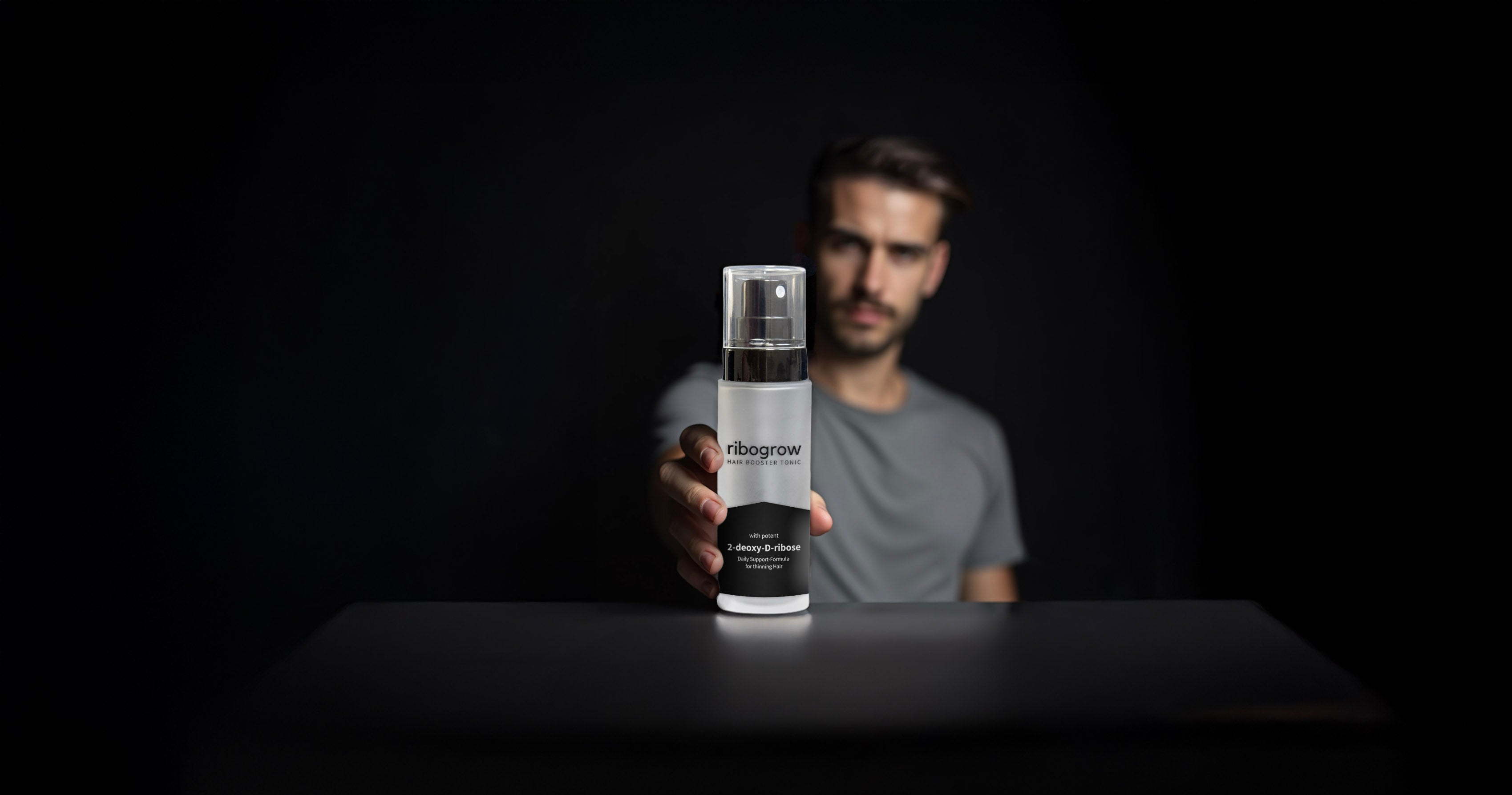 Mann hält das ribogrow Hair Booster Tonic in den Händen vor schwarzem Hintergrund – Premium-Haarwuchstonikum für kräftigeres und gesünderes Haar. Bannerbild für maximale Sichtbarkeit.