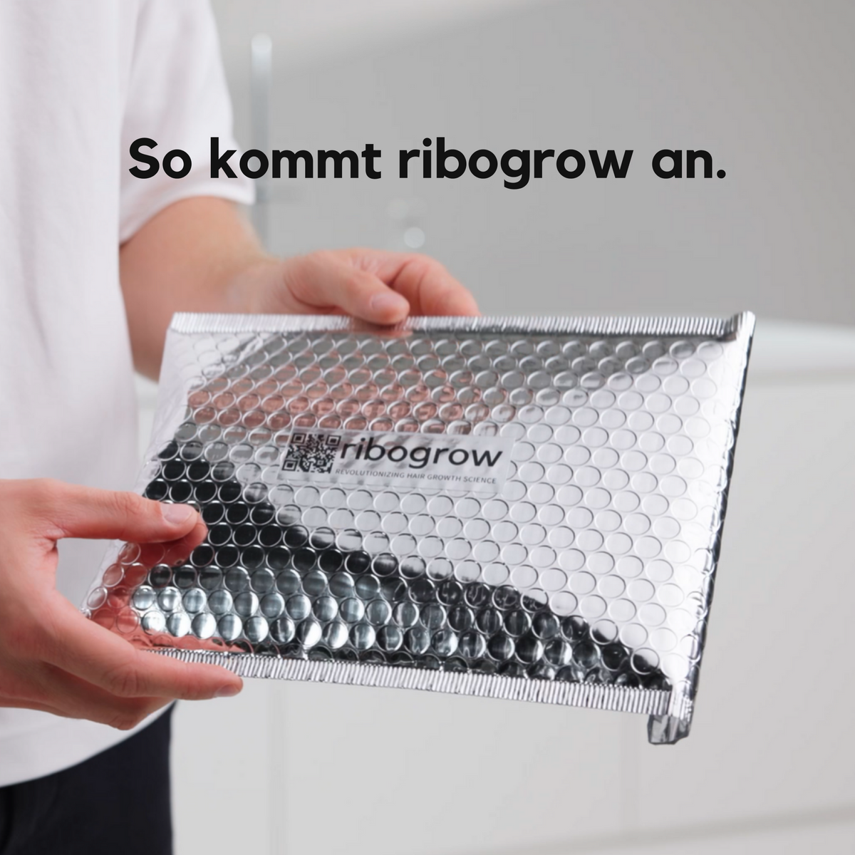 ribogrow® Lieferung: Eine Person hält einen silbernen, gepolsterten Versandumschlag mit ribogrow®-Logo und QR-Code. Die hygienische, diskrete Verpackung zeigt, wie das Haarwuchsmittel sicher beim Kunden ankommt.