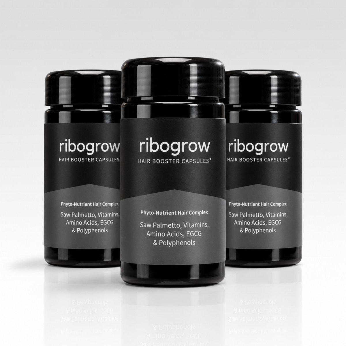 Drei schwarze ribogrow® Hair Booster Capsules Dosen mit glänzenden Schraubdeckeln und grau-schwarzen Etiketten. Die Nahrungsergänzungsmittel enthalten einen Phyto-Nährstoff-Komplex mit Sägepalme, Vitaminen, Aminosäuren, EGCG und Polyphenolen. Die Dosen sind versetzt vor einem hellgrauen Hintergrund auf einer spiegelnden weißen Oberfläche angeordnet.
