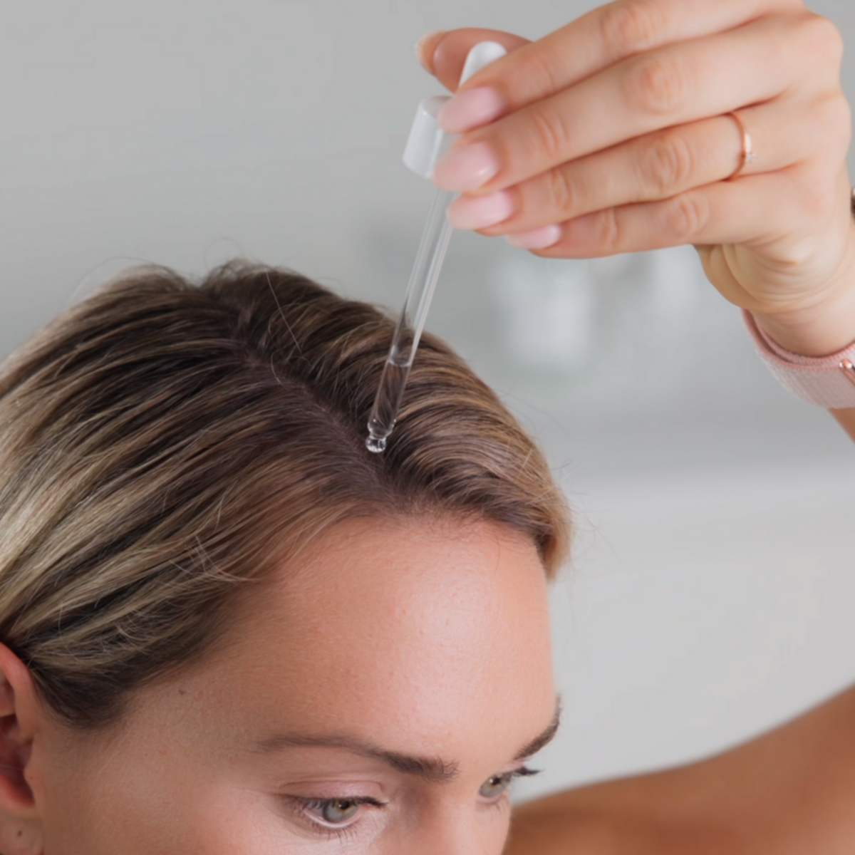 Zeigt die Pipettenanwendung des Hair Booster Serums auf der Kopfhaut bei einem weiblichen Model