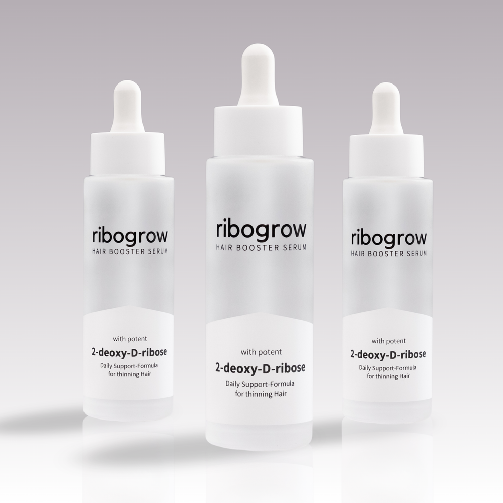 Drei Flaschen ribogrow® Hair Booster Serum mit Pipettenverschluss, in mattem Glasdesign, auf hellem, dezent verlaufendem Hintergrund nebeneinander angeordnet.
