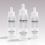 Drei Flaschen ribogrow Hair Booster Serum mit Pipettenverschluss, in mattem Glasdesign, auf hellem, dezent verlaufendem Hintergrund nebeneinander angeordnet.