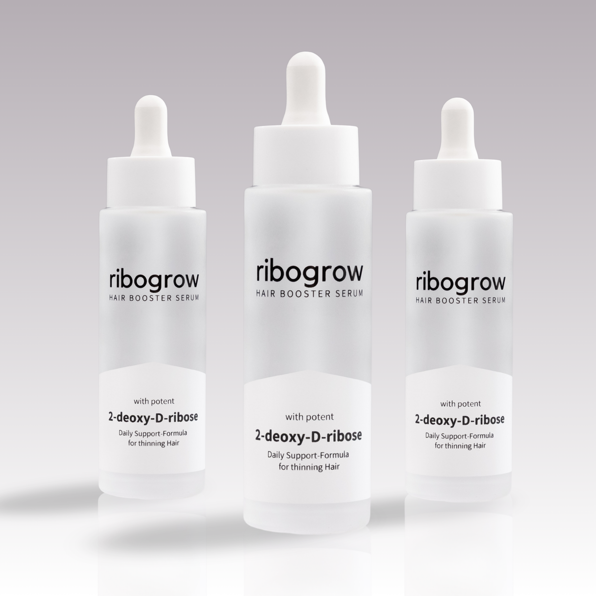 Drei Flaschen ribogrow Hair Booster Serum mit Pipettenverschluss, in mattem Glasdesign, auf hellem, dezent verlaufendem Hintergrund nebeneinander angeordnet.