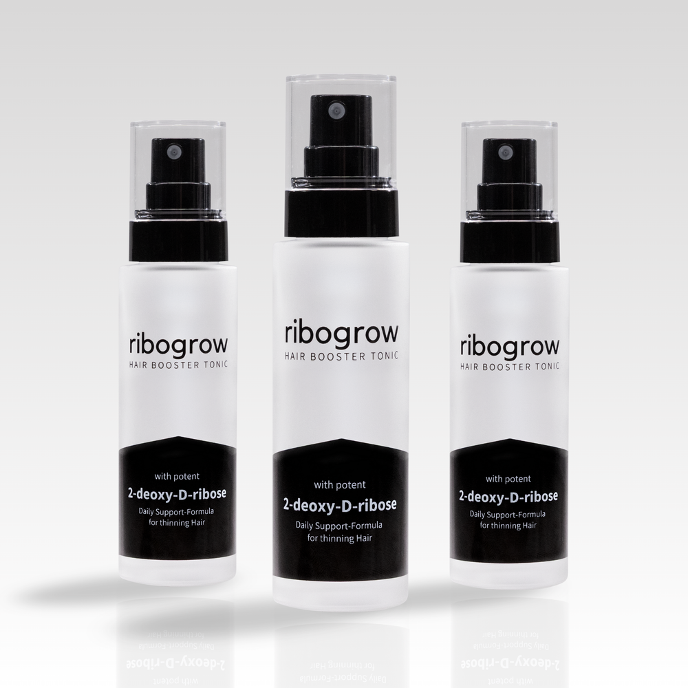 Drei Flaschen ribogrow® Hair Booster Tonic aus mattem Glas mit schwarzem Sprühkopf und transparenter Kappe, nebeneinander auf hellem Hintergrund angeordnet.