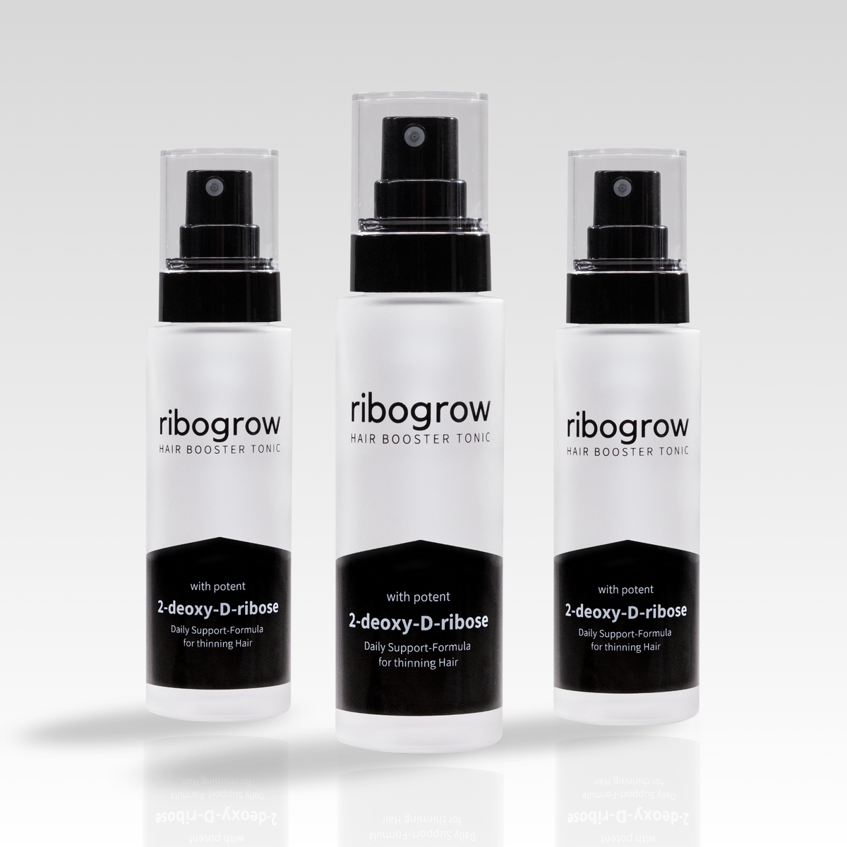 Drei Flaschen ribogrow Hair Booster Tonic aus mattem Glas mit schwarzem Sprühkopf und transparenter Kappe, nebeneinander auf hellem Hintergrund angeordnet.