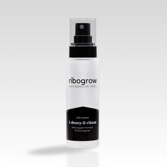Einzelne Flasche ribogrow Hair Booster Tonic aus mattem Glas mit schwarzem Sprühkopf und transparenter Kappe, auf hellem, weich verlaufendem Hintergrund stehend.